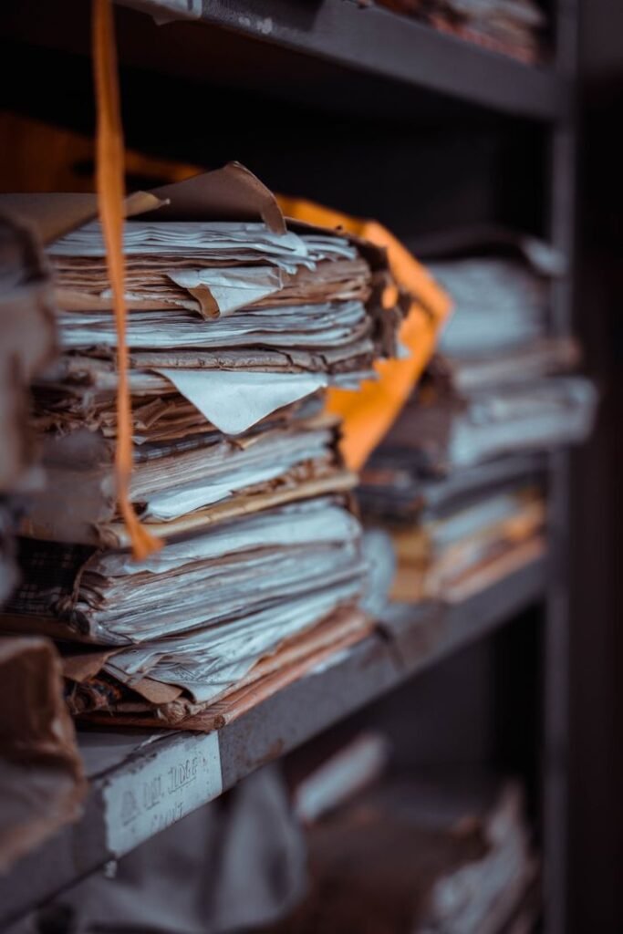 pexels-photo-3927131 Stacks of old documents and papers piled on dusty shelves, creating an organized yet chaotic scene.